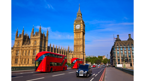 Tall building with a clock at the top and double decker buses driving on the road